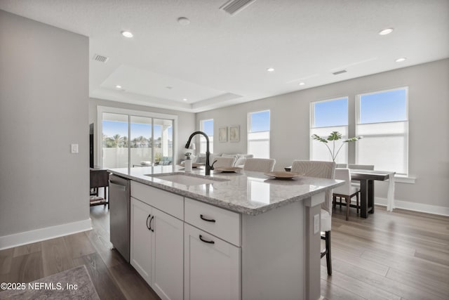 kitchen featuring sink, light stone counters, an island with sink, white cabinets, and stainless steel dishwasher