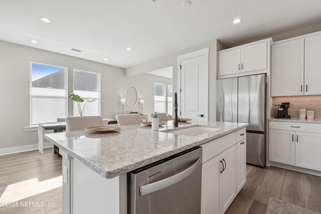 kitchen with sink, stainless steel appliances, white cabinets, a center island with sink, and light wood-type flooring