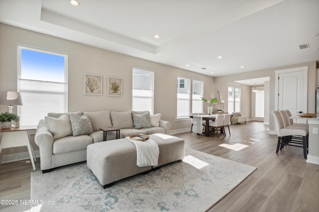 living room with a tray ceiling and light hardwood / wood-style flooring