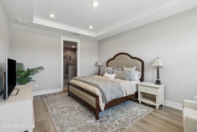 bedroom featuring ensuite bathroom, a tray ceiling, hardwood / wood-style floors, and a textured ceiling