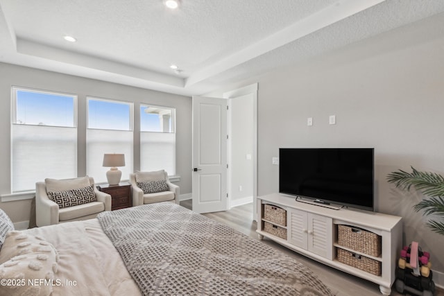 bedroom with a tray ceiling, a textured ceiling, and light wood-type flooring