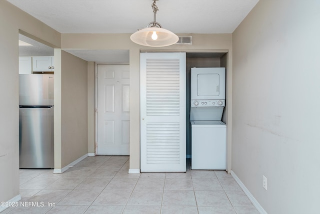 laundry room featuring stacked washer and dryer, light tile patterned floors, and a textured ceiling