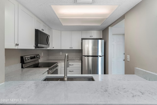 kitchen with light stone counters, appliances with stainless steel finishes, sink, and white cabinets