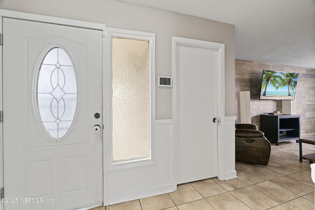 entryway with wooden walls, a textured ceiling, and light tile patterned floors