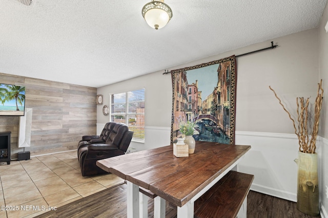 dining space featuring wood-type flooring, wooden walls, and a textured ceiling