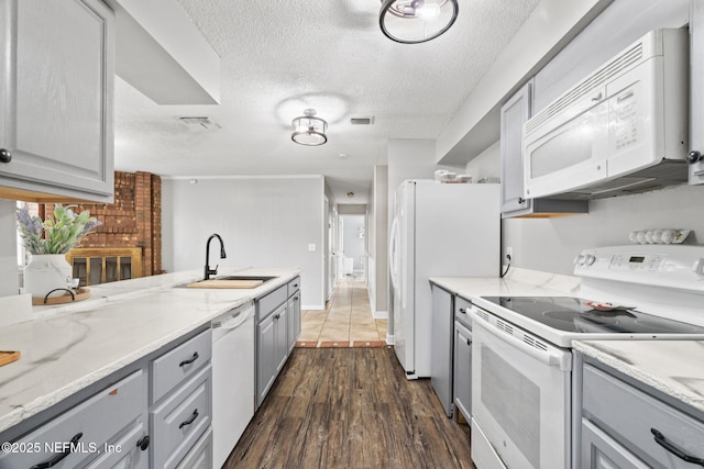 kitchen with dark wood-type flooring, sink, gray cabinetry, white appliances, and light stone countertops