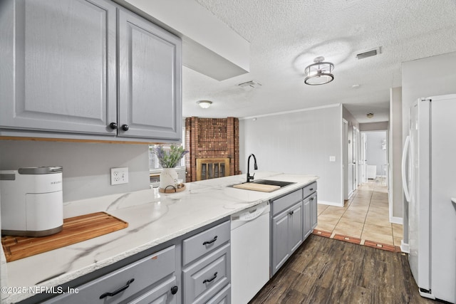 kitchen with sink, a textured ceiling, dark hardwood / wood-style flooring, gray cabinets, and white appliances