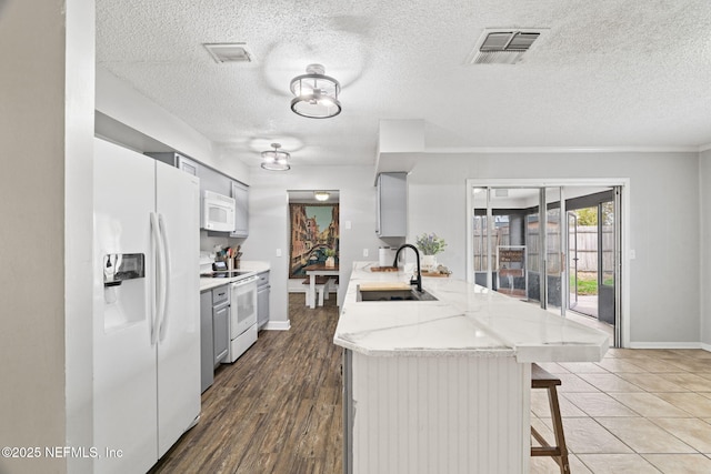 kitchen featuring a breakfast bar, sink, light stone counters, a textured ceiling, and white appliances