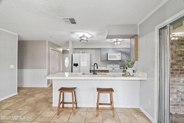 kitchen featuring sink, white appliances, gray cabinets, a kitchen bar, and kitchen peninsula