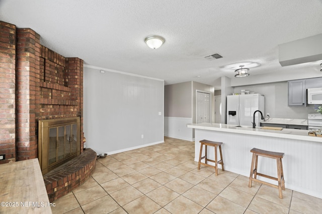 kitchen with gray cabinets, sink, a kitchen bar, a brick fireplace, and white appliances