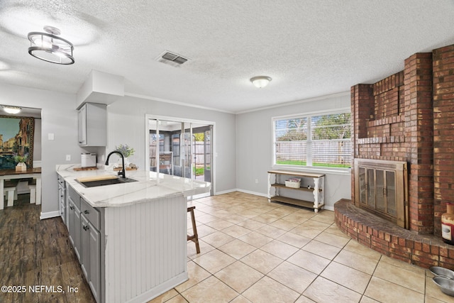 kitchen featuring light tile patterned floors, sink, a textured ceiling, a brick fireplace, and kitchen peninsula