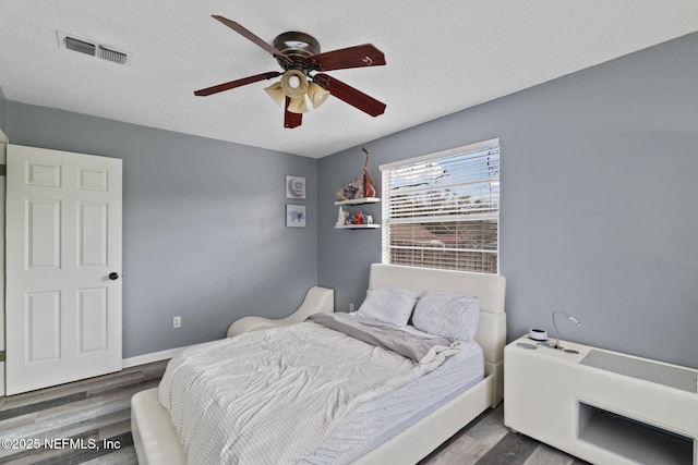 bedroom featuring dark hardwood / wood-style flooring, ceiling fan, and a textured ceiling