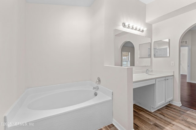 bathroom with hardwood / wood-style floors, vanity, and a relaxing tiled tub