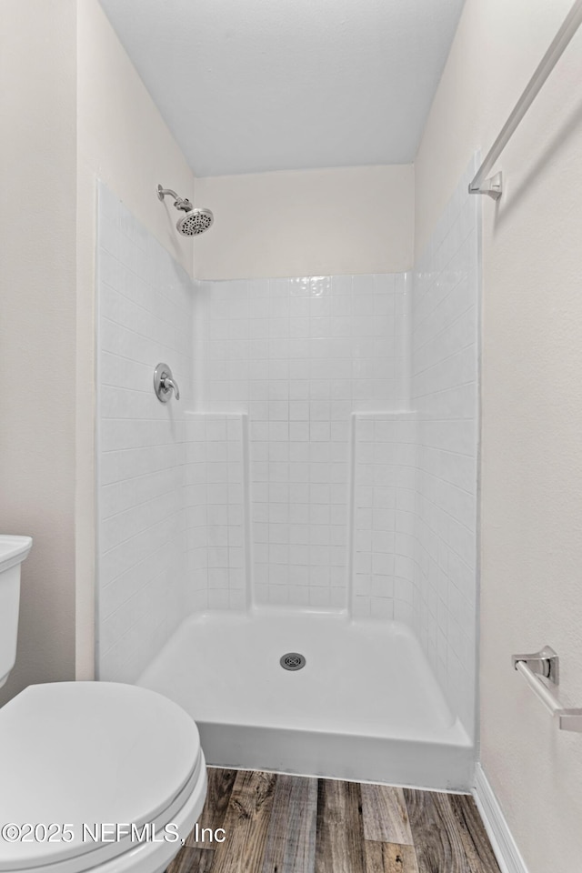 bathroom with hardwood / wood-style flooring, a tile shower, and toilet