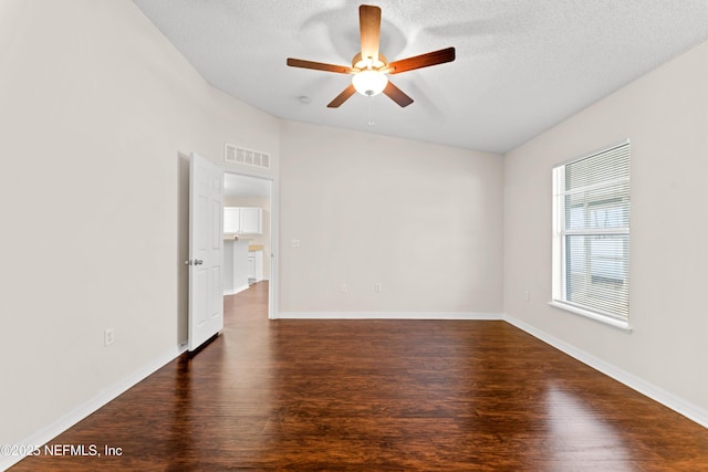 empty room featuring ceiling fan, dark wood-type flooring, and a textured ceiling