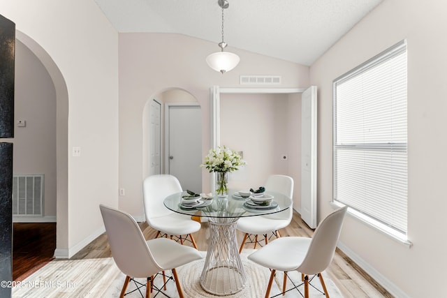 dining room featuring lofted ceiling, light hardwood / wood-style flooring, and a textured ceiling