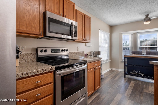 kitchen with a textured ceiling, appliances with stainless steel finishes, dark hardwood / wood-style flooring, ceiling fan, and dark stone counters