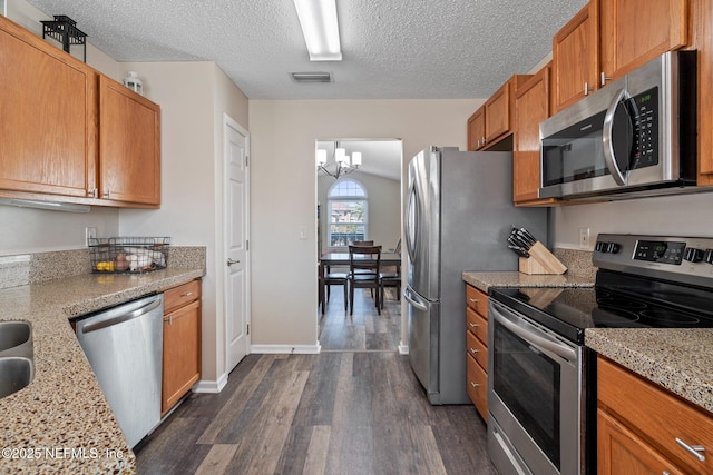 kitchen with dark wood-type flooring, light stone counters, a textured ceiling, appliances with stainless steel finishes, and a notable chandelier