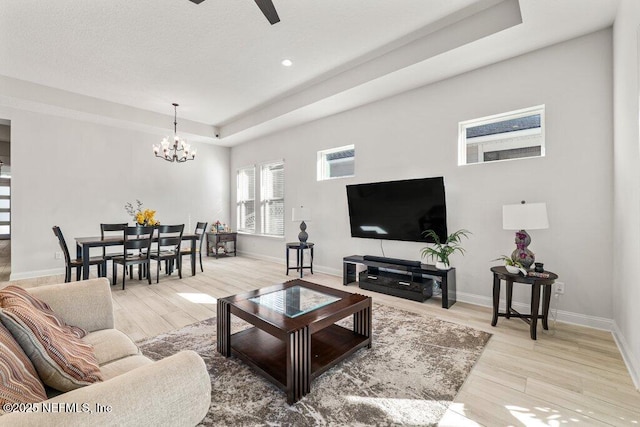 living room featuring a raised ceiling, ceiling fan with notable chandelier, and light hardwood / wood-style floors