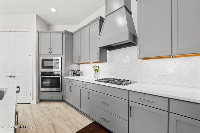 kitchen with gray cabinetry, custom exhaust hood, light stone countertops, and appliances with stainless steel finishes