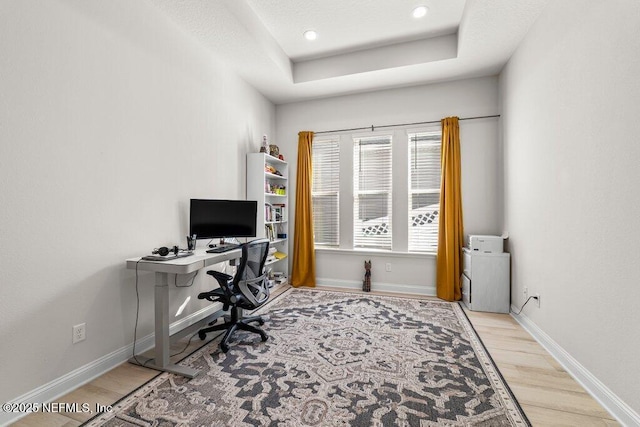 office space featuring a tray ceiling and light wood-type flooring