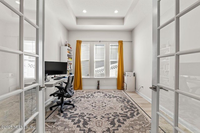 office space with a raised ceiling, light wood-type flooring, and french doors