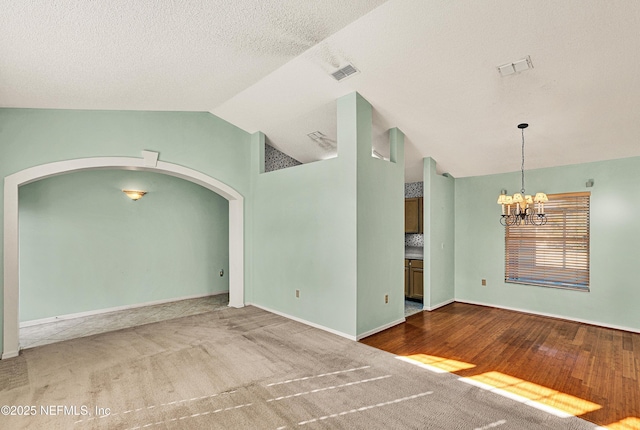 carpeted spare room with lofted ceiling, a textured ceiling, and an inviting chandelier