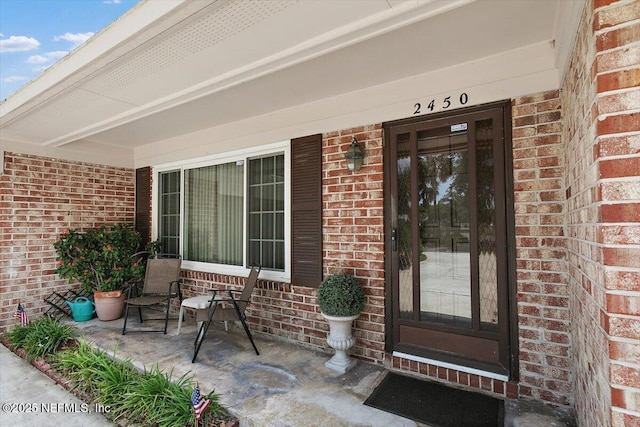 view of exterior entry featuring brick siding and covered porch
