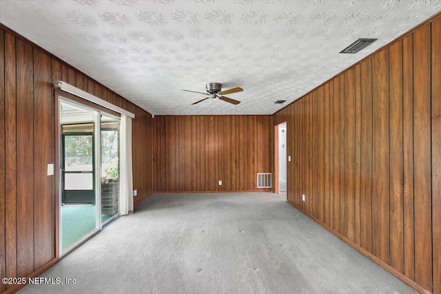 spare room with wooden walls, ceiling fan, visible vents, and light carpet