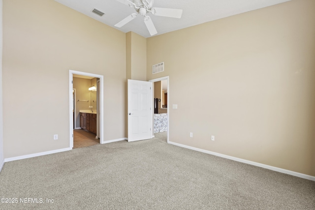 unfurnished bedroom featuring ceiling fan, ensuite bathroom, high vaulted ceiling, and light carpet