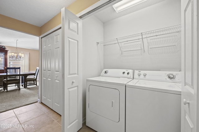 laundry area with an inviting chandelier, light tile patterned floors, a textured ceiling, and washer and clothes dryer