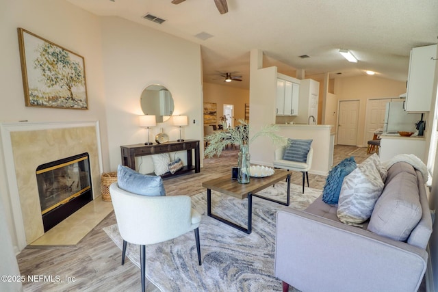 living room featuring ceiling fan, lofted ceiling, a high end fireplace, and light hardwood / wood-style flooring