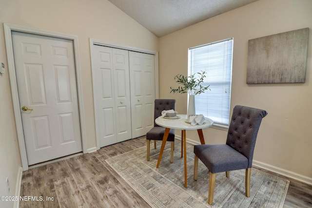 dining room featuring light hardwood / wood-style floors, vaulted ceiling, and a textured ceiling