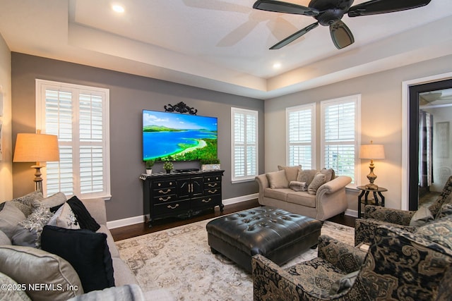 living room with a raised ceiling, dark wood-type flooring, and ceiling fan