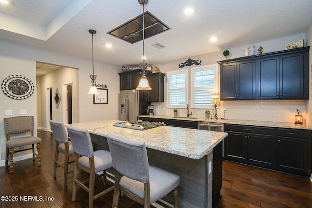 kitchen featuring a kitchen island, decorative light fixtures, tasteful backsplash, sink, and dark wood-type flooring