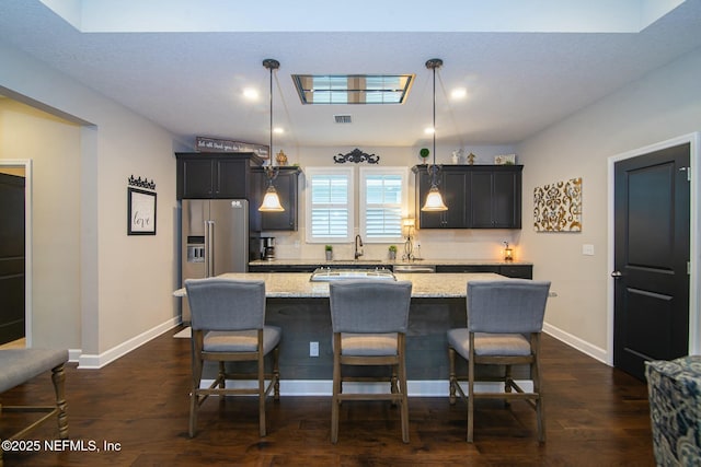 kitchen with a breakfast bar, hanging light fixtures, a center island, light stone counters, and high quality fridge