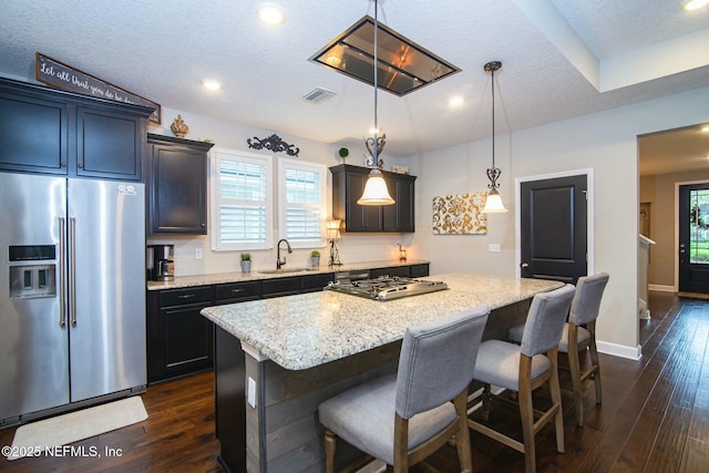 kitchen featuring a kitchen island, appliances with stainless steel finishes, sink, hanging light fixtures, and light stone countertops