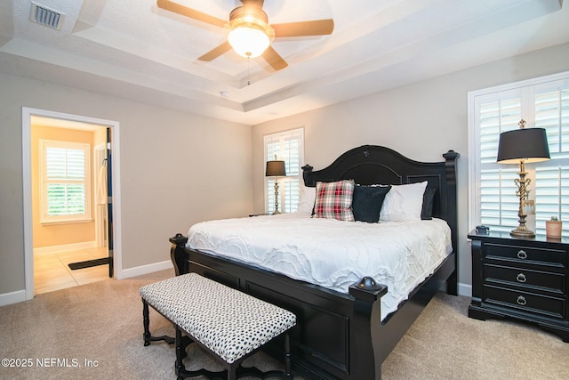 bedroom with light colored carpet, connected bathroom, and a tray ceiling