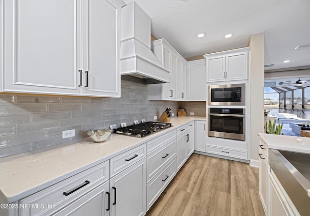 kitchen featuring white cabinetry, stainless steel appliances, tasteful backsplash, custom exhaust hood, and light wood-type flooring