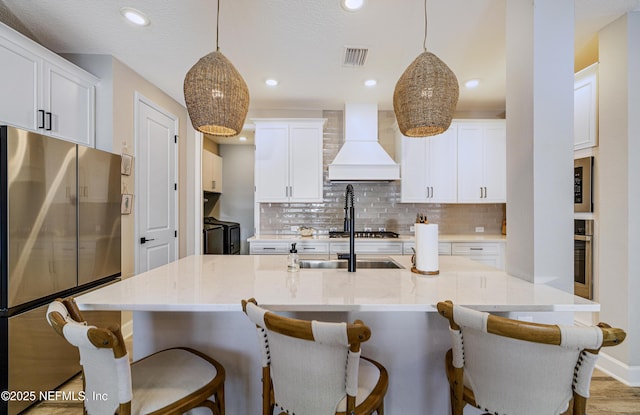 kitchen featuring custom exhaust hood, appliances with stainless steel finishes, independent washer and dryer, and decorative light fixtures