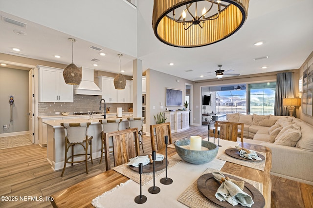 living room with ceiling fan with notable chandelier, sink, and light hardwood / wood-style floors