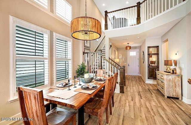 dining space featuring a towering ceiling, light hardwood / wood-style flooring, and a wealth of natural light