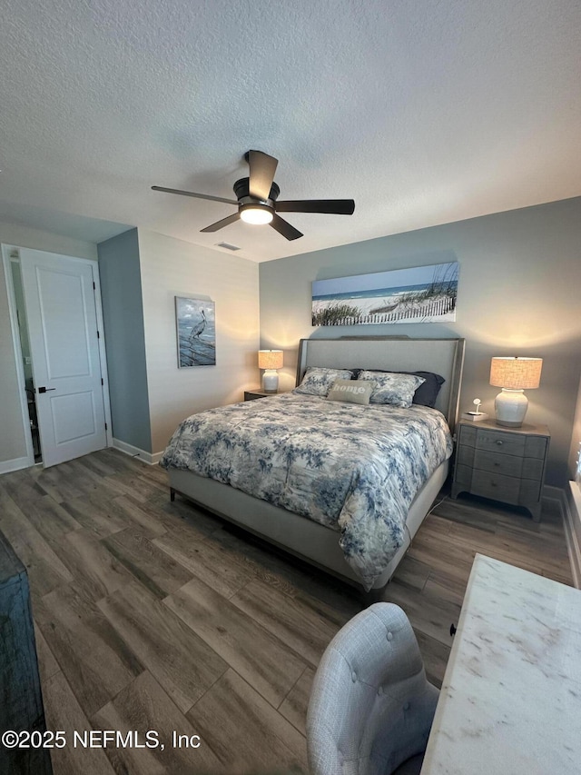 bedroom with ceiling fan, wood finished floors, baseboards, and a textured ceiling