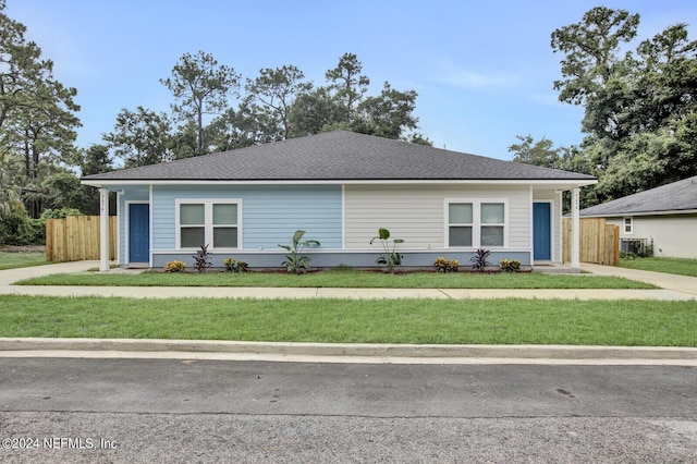 ranch-style home featuring roof with shingles, fence, and a front yard