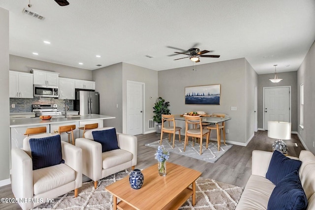 living room with ceiling fan, wood finished floors, visible vents, and baseboards