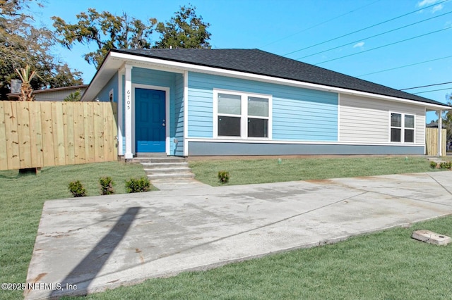 view of front facade featuring a shingled roof, entry steps, fence, and a front lawn