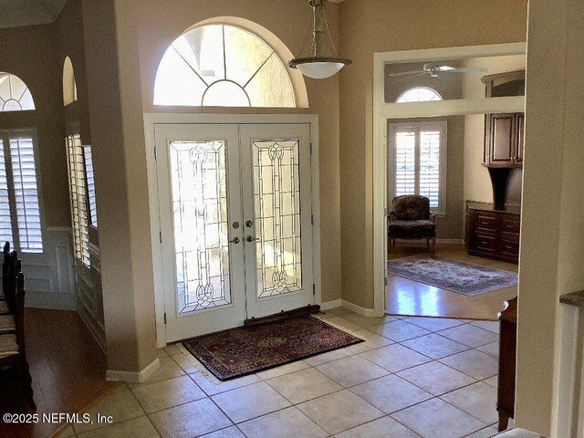 entryway with a towering ceiling, light tile patterned floors, baseboards, and french doors