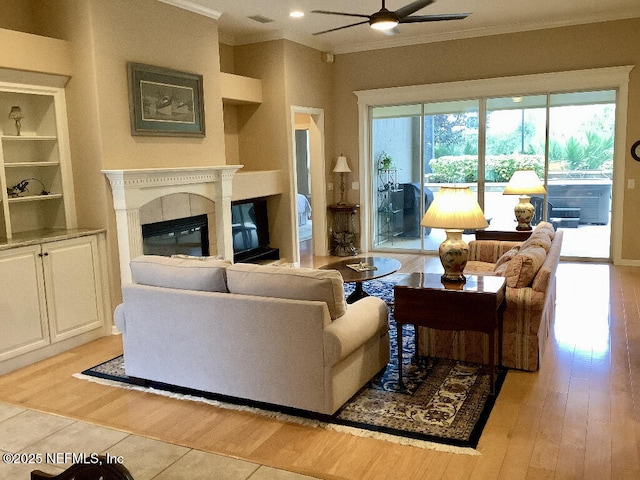 living area featuring light wood finished floors, a glass covered fireplace, visible vents, and crown molding