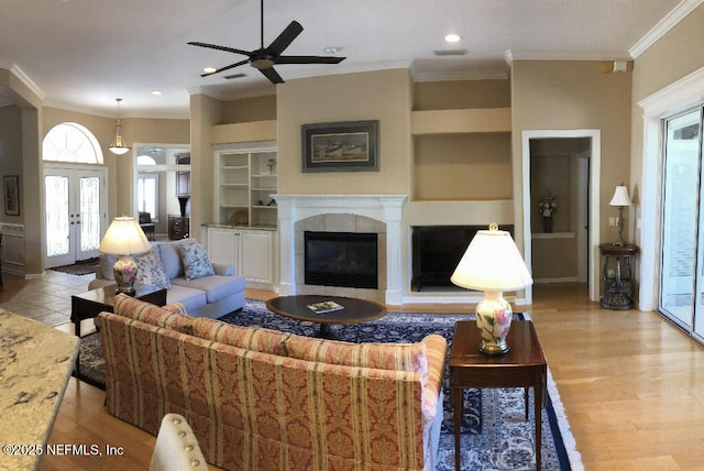 living area featuring a tile fireplace, ornamental molding, french doors, light wood-style floors, and built in shelves