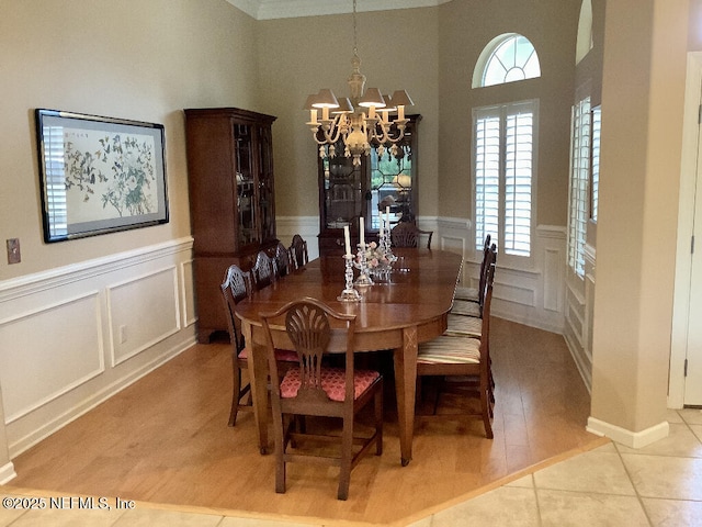 dining area featuring light tile patterned floors, a decorative wall, wainscoting, and a notable chandelier